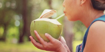 Žena pije brčkem vodu z mladého kokosu, který drží v dlaních