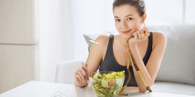 Žena drží metr a jí zeleninový salát