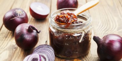 Cibulová marmeláda ve sklenici a červené cibule kolem ní