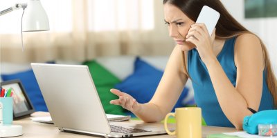 Naštvaná, zmatená žena sedí u notebooku a telefonuje