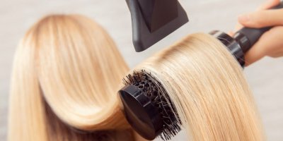 Ženské vlasy, které kadeřnice fénuje a pročesává kartáčem