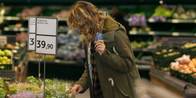 Žena v obchodě si prohlíží bazalku a v ruce drží stravenkovou kartu Benefitka