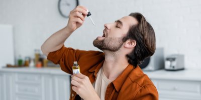 Muž drží lahvičku CBD kapek a kape si do úst