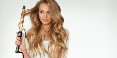 Žena si natáčí dlouhé, blonďaté vlasy kulmou s klipem