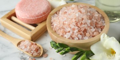 Růžová sůl v dřevěné misce, v pozadí růžové mýdlo