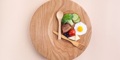 Talíř, lžíce a vidlička jsou umístěny tak, aby tvořily hodiny, v úhlu, který svírají hodinové ručičky, je brokolice, rajče, vejce, sýr