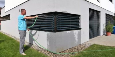 Muž sprchuje žaluzie zahradní hadicí