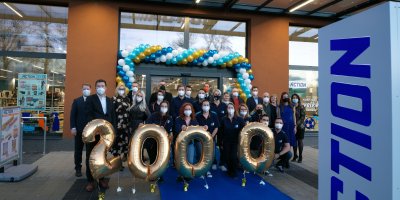 Firemní fotografie výroční akce společnosti Action, zaměstnanci stojí před obchodem a před sebou mají balonky ve tvaru čísla 2 000