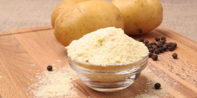 Instantní bramborová kaše v misce, za ní brambory a koření