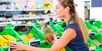 Žena doplňuje zeleninu do regálů v supermarketu