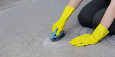 Ruce v gumových rukavicích čistí koberec houbičkou