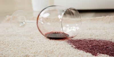 Sklenička červeného vína rozlitá na koberci