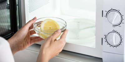 Člověk vkládá misku s vodou a citronem do mikrovlnné trouby
