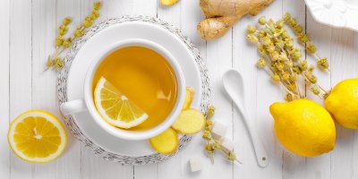 Šálek čaje, ve kterém je polovina plátku citronu, kolem citrony, zázvor, lžička, cukr, bylinky
