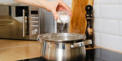 Ruka drží solničku a solí vodu v hrnci