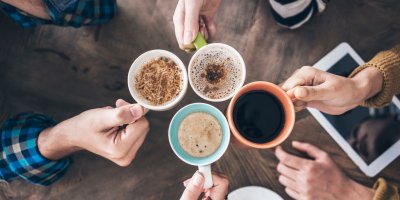 Skupina lidí si přiťukává šálky s různými druhy kávy