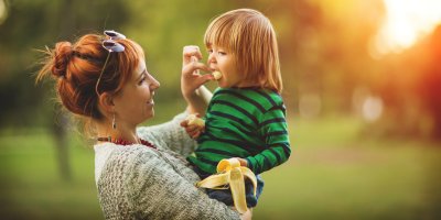 Žena drží dítě v náruči a krmí ho banánem