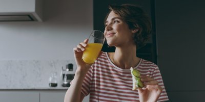 Žena se usmívá a drží v ruce džus a chleba s okurkou