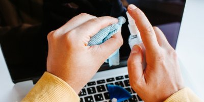 Muž čistí notebook sprejem a hadříkem