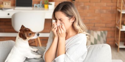 Žena má alergickou rýmu a smrká do kapesníku, vedle ní leží pes
