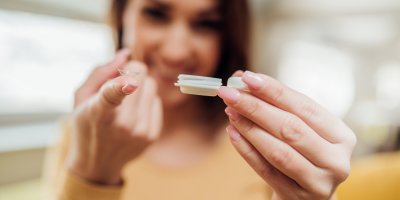 Žena drží v ruce pouzdro na čočky a na prstu má kontaktní čočku