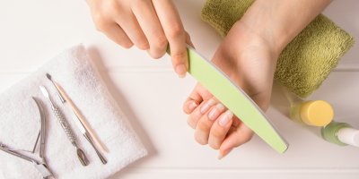 Žena si piluje nehty, na ručníku má vyskládané další pomůcky na manikúru