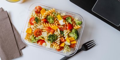 Krabička s těstovinami a zeleninou vedle notebooku