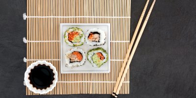 Čtyři kousky sushi na talíři, sójová omáčka v mističce, hůlky