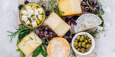 Různé druhy sýrů, olivy, ostružiny a bylinky na prostírání