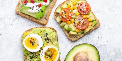 Tři avokádové toasty, jeden s vejcem, druhý s rajčaty a kukuřicí a třetí s granátovým jablkem