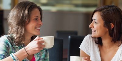 Dvě ženy drží hrnky a usmívají se u toho