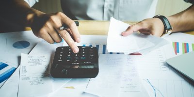 Muž prochází dokumenty s financemi a počítá na kalkulačce