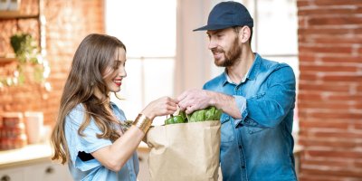 Kurýr předává ženě papírovou tašku s nákupem