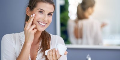 Žena se usmívá a nanáší si krém na tvář