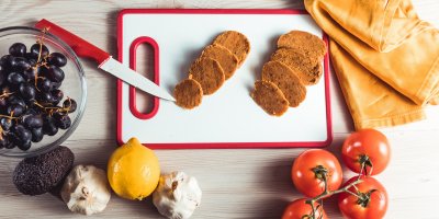 Nakrájený seitan na prkénku, kolem jsou rajčata, hroznové víno, citron, česnek, avokádo, nůž, utěrka