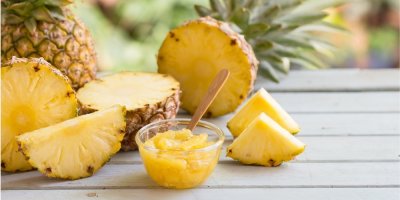 Nakrájený ananas v misce, v pozadí větší kousky ananasu