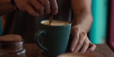 Mužské ruce lžičkou promíchávají šálek kávy.