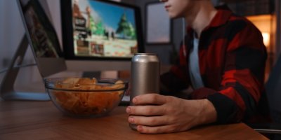 Mladý muž sedí u počítače s energy drinkem v plechovce.