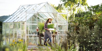 Mladá žena vychází ze skleníku s květináčem