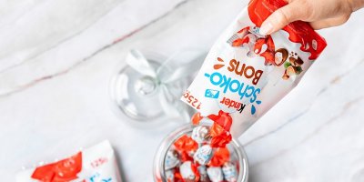 Ruka vysypává čokoládové bonbony Kinder do dózy