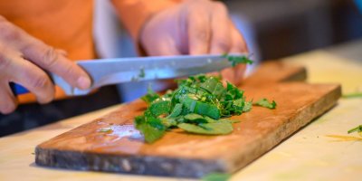 Ruka držící nůž a nakrájené kopřivy na dřevěném prkénku