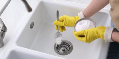 Člověk v gumových rukavicích čistí dřez pomocí jedlé sody