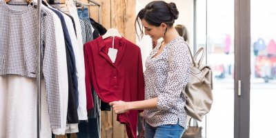 Žena si v obchodě prohlíží červenou blůzu