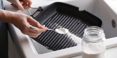 Člověk sype jedlou sodu na připálenou pánev