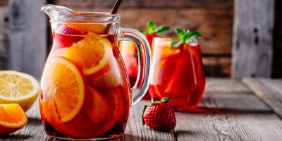 Sangría z červeného vína, jahod a pomerančů ve džbánu, v pozadí dvě plné skleničky