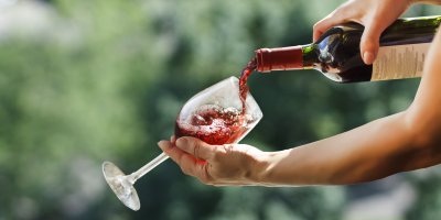 Žena nalévá červené víno z lahve do sklenice