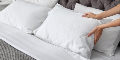 Žena načechrává polštáře v posteli