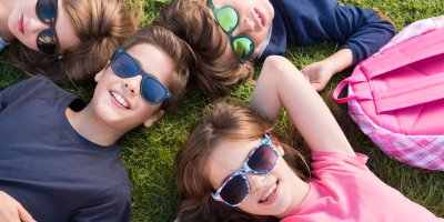Čtyři děti leží na trávě a na očích mají sluneční brýle