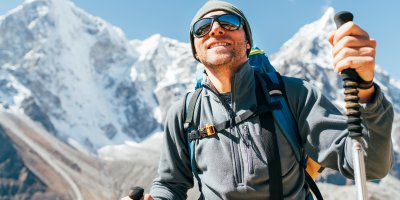 Muž se slunečními brýlemi, batohem a trekingovými holemi v horách