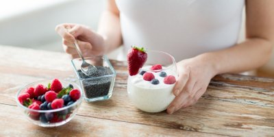 Detail na ruce žena, která si dává chia semínka do jogurtu s ovocem